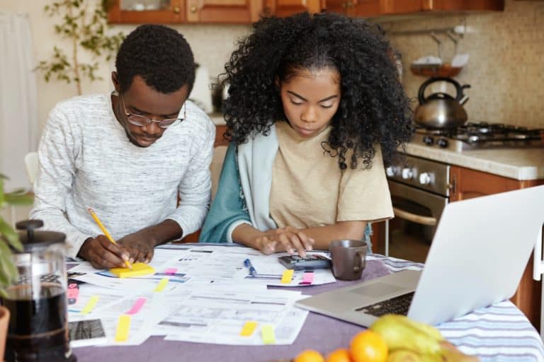 African man and woman sitting at kitchen table with papers and laptop pc, managing domestic finances