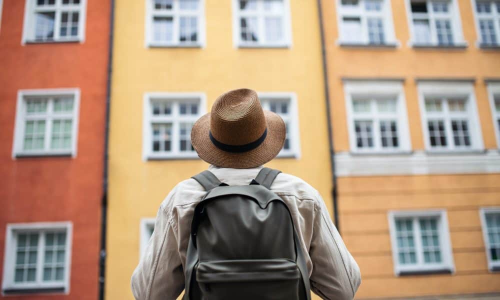 Rear view of senior man tourist outdoors looking at apartment building