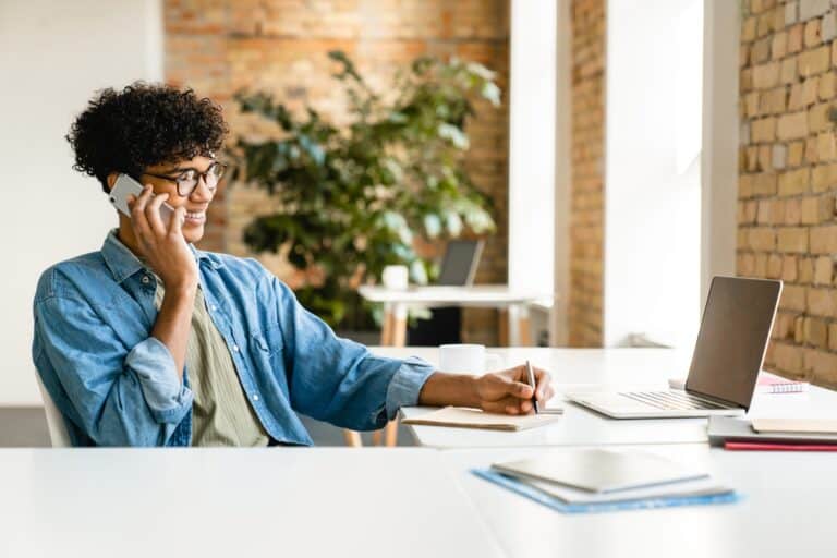 Successful young african man talking on phone while working at the desk in office