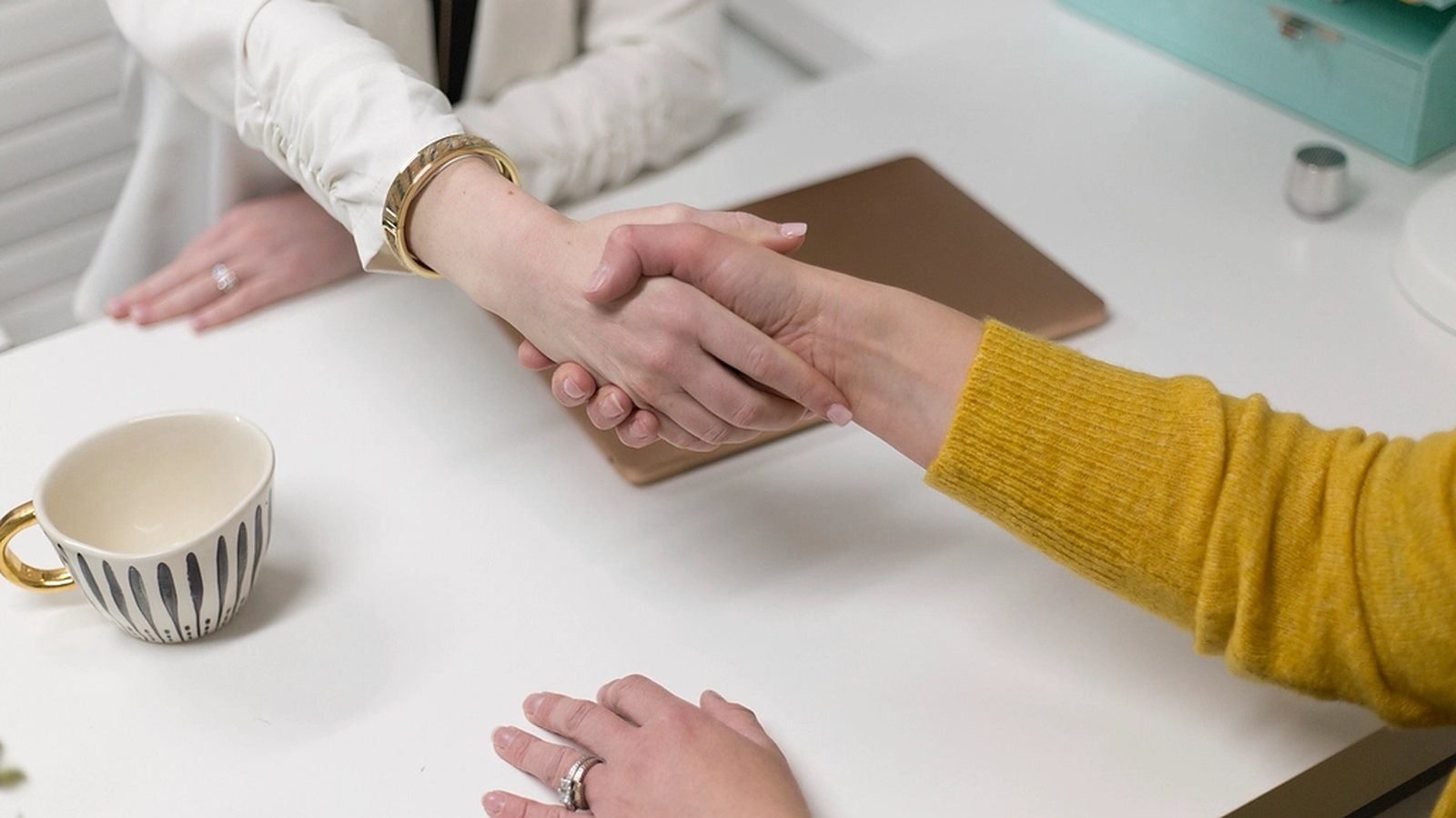 Two businesspeople shaking hands across a white desk