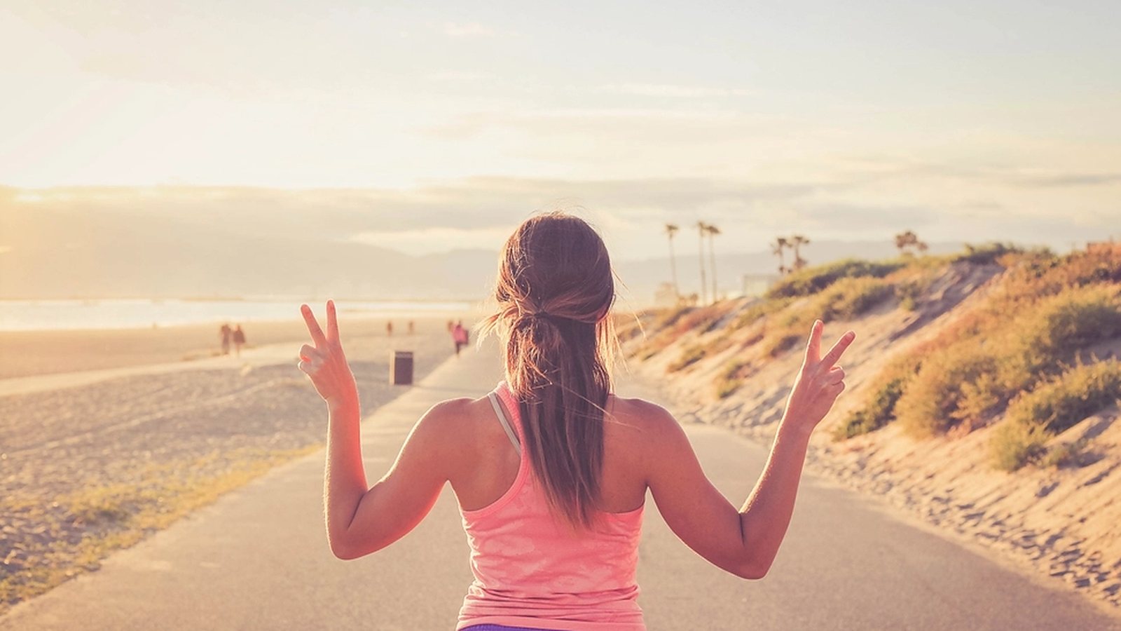 Woman in a pink sports top running along a beach path at sunset